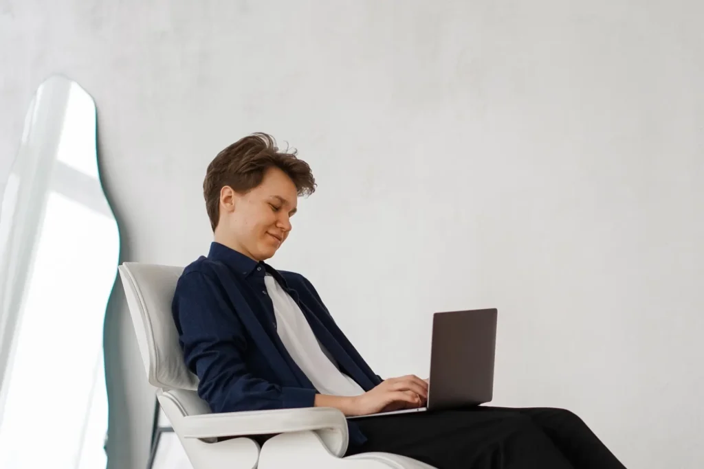 Fiatal férfi egy széken ül a laptopon dolgozik.